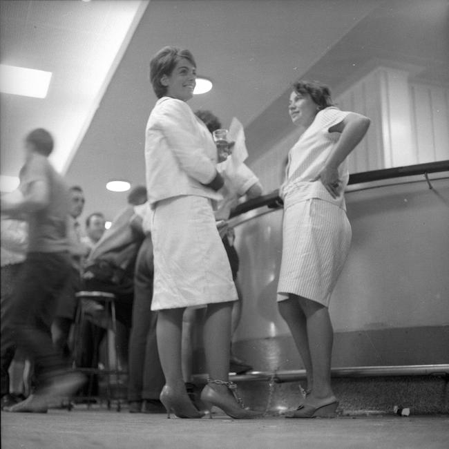 Chained to the footrail in the public bar of the Regatta Hotel, Toowong, are Mrs Rosalie Bogner, left, of Indooroopilly, and Merle Thornton of Fig Tree Pocket. The pair relaxed with a glass of beer bought for them by a hotel patron. They were drawing attention to their campaign to give women the right to drink side-by-side with men in public bars. Picture: Bruce Postle/The Courier-Mail