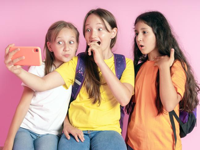 Three teen girls smiling and shoots a video on a pink background.  Selfies. Tiktok blogger.