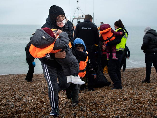 TOPSHOT - A migrant carries her children after being helped ashore from a RNLI (Royal National Lifeboat Institution) lifeboat at a beach in Dungeness, on the south-east coast of England, on November 24, 2021, after being rescued while crossing the English Channel. - The past three years have seen a significant rise in attempted Channel crossings by migrants, despite warnings of the dangers in the busy shipping lane between northern France and southern England, which is subject to strong currents and low temperatures. (Photo by Ben STANSALL / AFP)