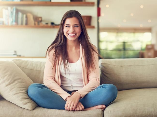 A cheerful young woman sitting at home on the couch. She has a mortgage on her first home. Picture: iStock.