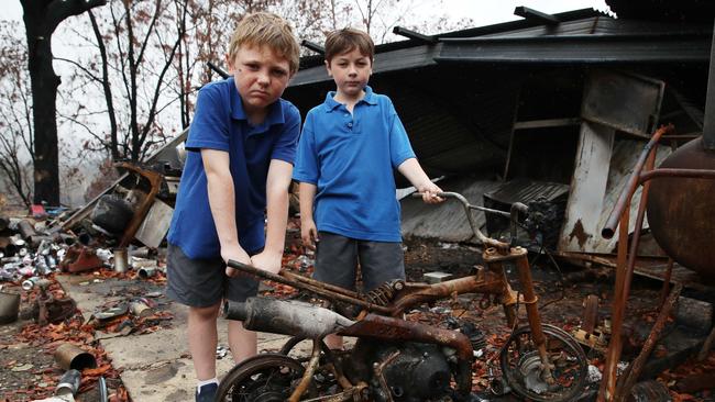 Braiden, 8, left, and Logan, 7, in the burnt remains of their home. Picture: David Swift