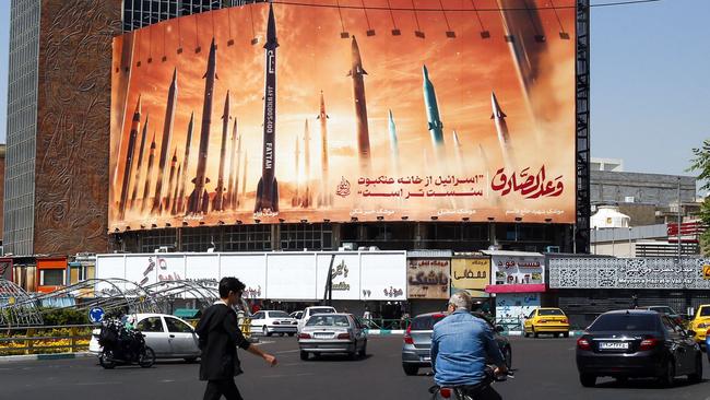 A man crosses a street as motorists drive past a billboard depicting Iranian ballistic missiles in service in Tehran on April 19. Picture: AFP