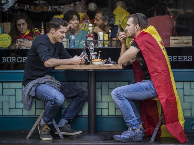 Two men, one draped in a Spanish flag, have lunch at a restaurant in downtown Barcelona after a mass rally against Catalonia's declaration of independence. Picture: Santi Palacios/AP