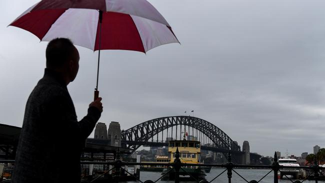 A man is seen walking in the rain in front of the Sydney Harbour Bridge during wet weather at Circular Quay. Picture: Bianca De Marchi