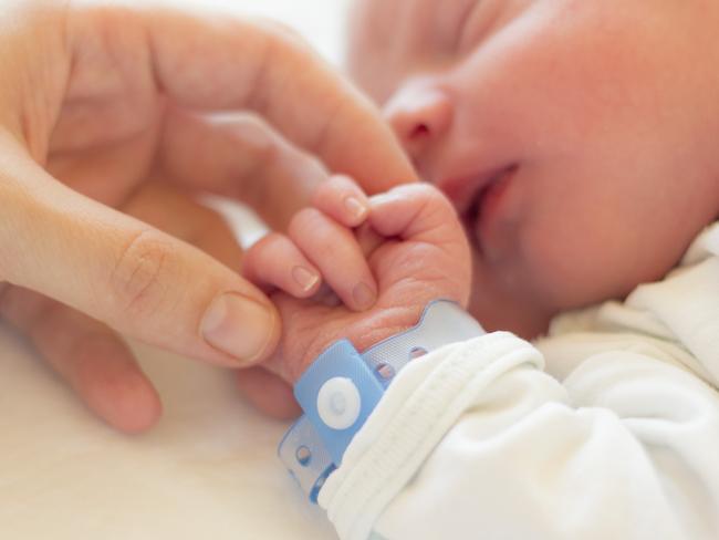 Newborn baby boy sleeping in his crib, his mother's hand holding his little hand.