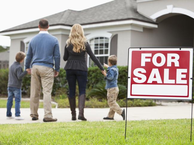 Family with two boys (4 and 6 years) standing in front of house with FOR SALE sign in front yard.  Focus on sign.