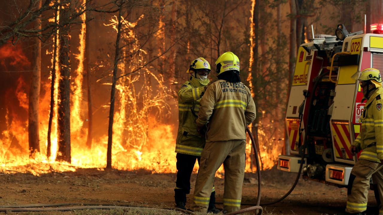 Firefighters hold back a fire threatening a house on The Buckets Way at Tinonee near Taree on the NSW mid north coast. Picture Nathan Edwards.