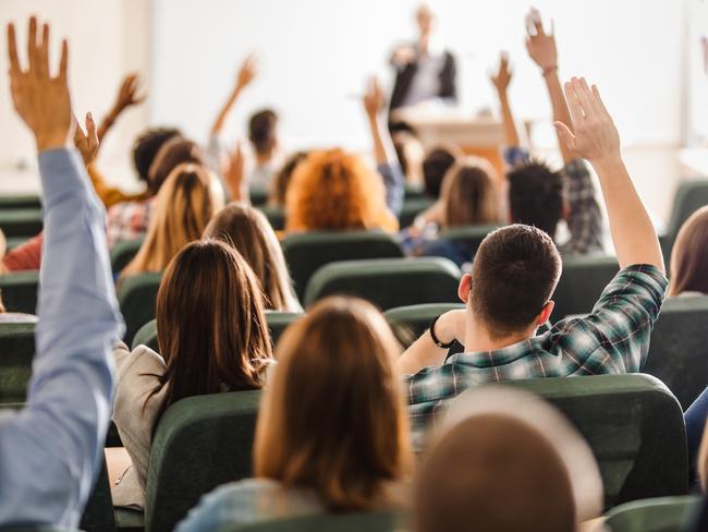 Back view of college students raising their arms on a class at lecture hall.