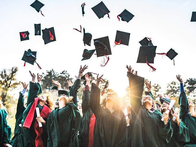 Large group of happy college students celebrating their graduation day outdoors while throwing their caps up in the air.