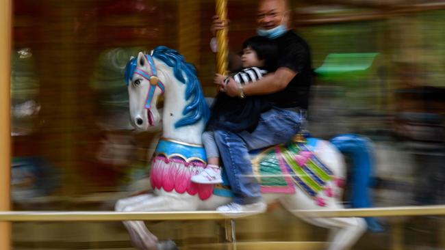 A man wearing a face mask as a preventive measure against the COVID-19 coronavirus holds his child on a horse carousel at Zhongshan Amusement Park in Wuhan. Picture: Hector Retamal/AFP