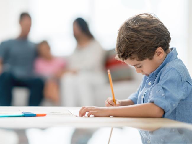 Portrait of a boy drawing and coloring at home with his family at the background - lifestyle concepts