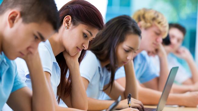 Schools of excellence - Row of private high school students work on assignment in class. They are writing or using laptops or digital tablets. They are concentrating as they study. They are wearing school uniforms.