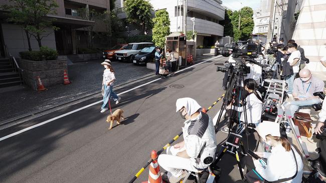 A woman (L) walks past members of the press gathered outside the residence of former Japanese prime minister Shinzo Abe in Tokyo. Picture: AFP