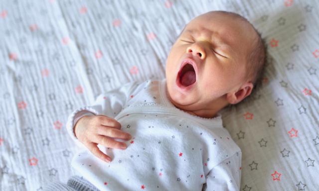 Adorable newborn baby girl sleeping and yawning in bed at home