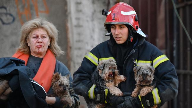 TOPSHOT – An emergency worker carries dogs as he escorts a local resident outside a partially destroyed multistorey office building after several Russian strikes hit the Ukrainian capital of Kyiv on October 10, 2022, amid Russia's invasion of Ukraine. – The head of the Ukrainian military said that Russian forces launched at least 75 missiles at Ukraine on Monday morning, with fatal strikes targeting the capital Kyiv, and cities in the south and west. (Photo by Sergei SUPINSKY / AFP)