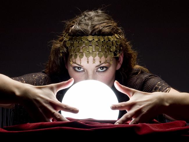 Mysterious focused fortune telling woman wearing a copper hair dress with her hands on a glowing crystal ball looking at the camera