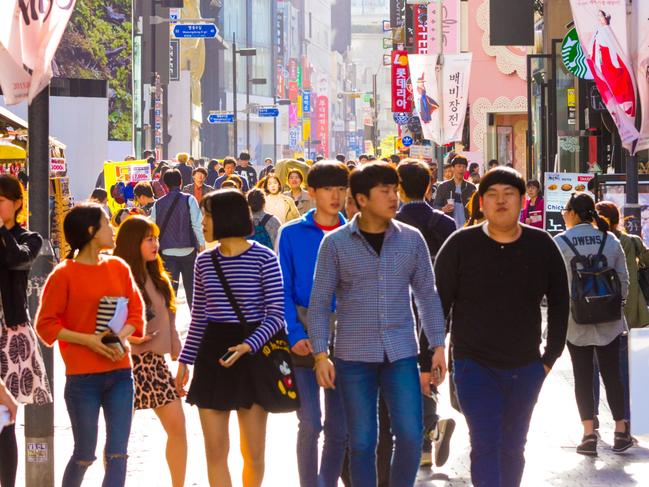 Seoul, South Korea - April 17, 2015: Young Koreans walking down busy backlit Myeongdong pedestrian shopping street with commercialism of many store signs and crowded with shoppers