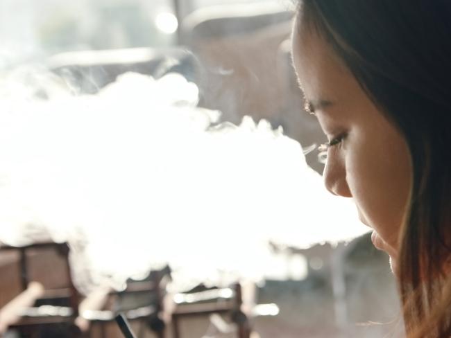 Shot of a young woman vaping at home