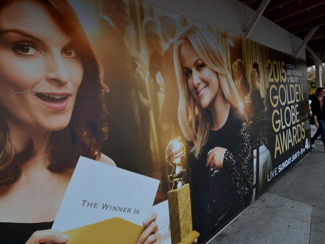 Commuters walk past a poster showing the Golden Globe Award hosts Tina Fey and Amy Poehler in Beverly Hills.