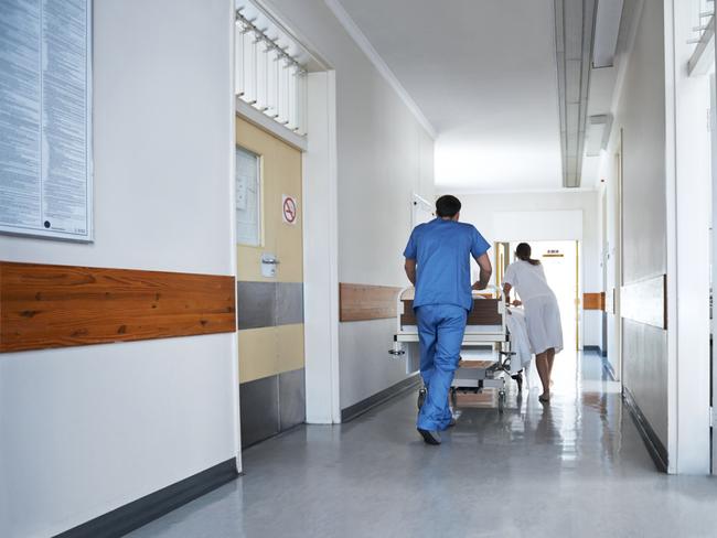 Rearview shot of hospital staff wheeling a patient in a gurney down a corridor