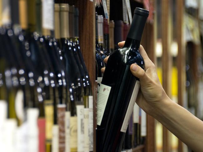 A woman's hand reaches out to select a bottle of red wine from the shelf of a wine shop