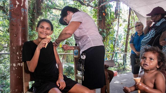 Sherrie Bligh, 19, enjoys her free ice cream as she is vaccinated by nurse Susie Jarman at her Yarrabah home with two-year-old Cleo Costello looking on. Picture: Brian Cassey