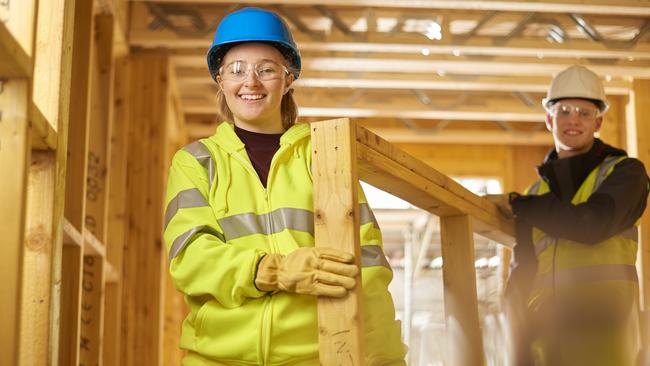 a female construction worker carries some studwork on a building site housing development and is assited by a male colleague .