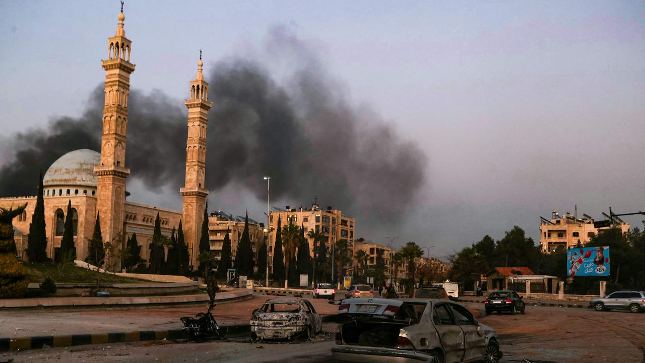 Smoke billows in the distance as damaged cars are seen at the site of Syrian regime air strikes targeting anti-regime fighters in Aleppo. Picture: AFP