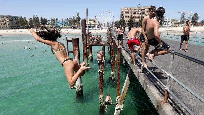 People jump off the Glenelg jetty on Monday. Temperatures are predicted to reach near-record levels this week. Picture: AAP / Kelly Barnes