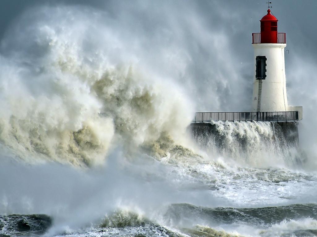 A waves breaks against a pier and a lighthouse in Les Sables-d’Olonne, western France, on February 9, 2016. High winds buffeted northwestern Europe on February 8, leaving one woman in France in a coma after she was hit by an advertising hoarding. Electricity was cut to 5,000 homes in northern France. / AFP / LOIC VENANCE