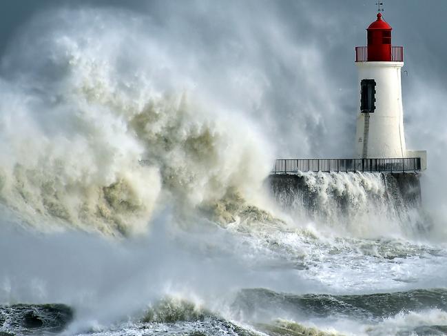 A waves breaks against a pier and a lighthouse in Les Sables-d’Olonne, western France, on February 9, 2016. High winds buffeted northwestern Europe on February 8, leaving one woman in France in a coma after she was hit by an advertising hoarding. Electricity was cut to 5,000 homes in northern France. / AFP / LOIC VENANCE