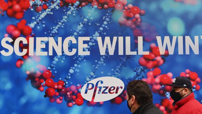 People wearing protective face masks walk past the Pfizer Inc. headquarters in New York City. Picture: AFP