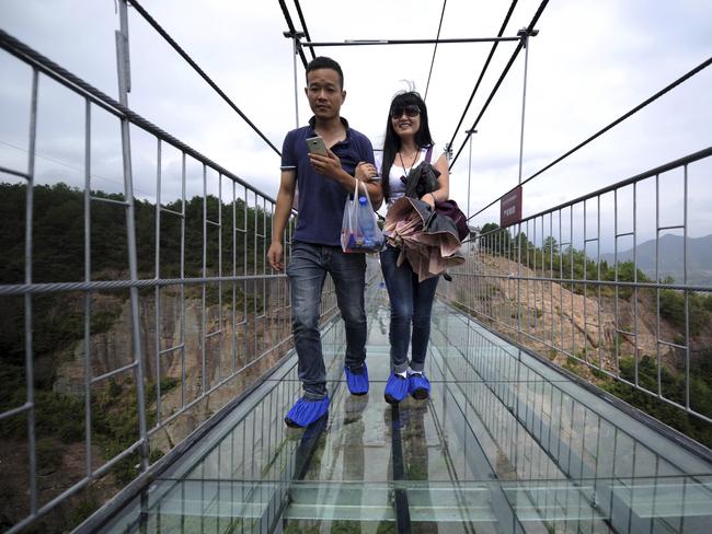 Visitors wear protective shoe coverings as they walk across the bridge. Picture: Chinatopix Via AP/ CHINA OUT