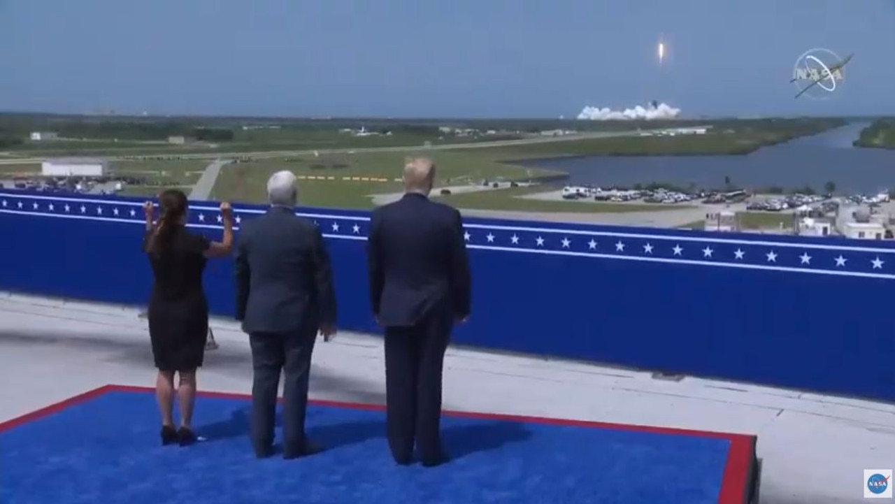 US President Donald Trump watches from a distance as the rocket takes off.