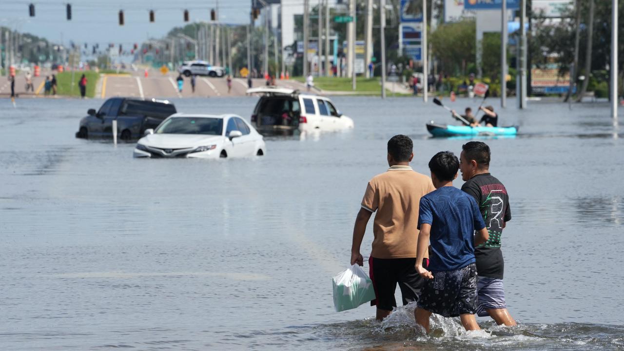 Kids walk past vehicles flooded in the water as the streets of the Southeast Seminole Heights section of Tampa due to Hurricane Milton on October 10, 2024 in Florida. Hurricane Milton tore a coast-to-coast path of destruction across the US state of Florida, whipping up a spate of deadly tornadoes that left at least four people dead, but avoiding the catastrophic devastation officials had feared. (Photo by Bryan R. SMITH / AFP)