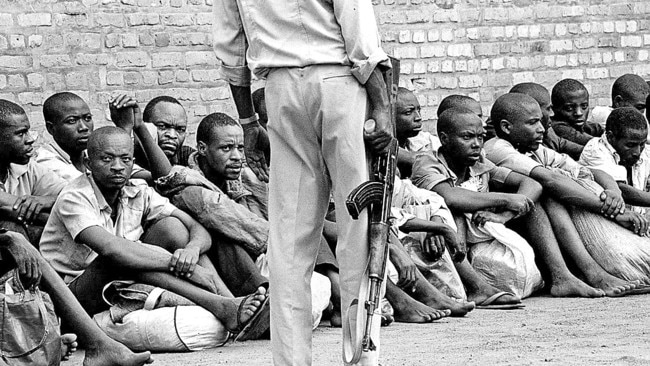 Arrested Hutu men accused of having participated in 1994 genocide line up waiting to enter Kibungo Prison under watchful eye of prison guard in 1997.