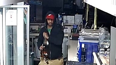 An unknown male wearing a dark hoodie, red cap, khaki shorts and red shoes is spotted in CCTV footage grabbing a large amount of liquor from the Jabiru Golf Club. Picture: NT PFES