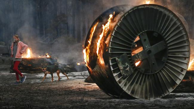 A young girl walks her dog past burning cable spools on a scorched property. Picture: David Caird