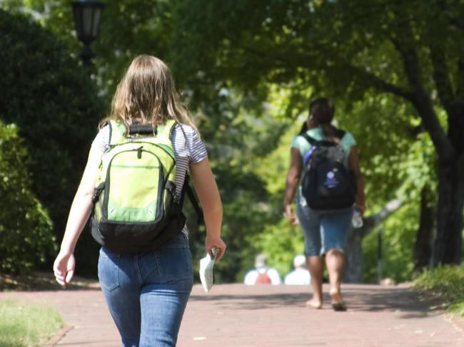 Generic of woman with backpack walking behind another student into college or university.