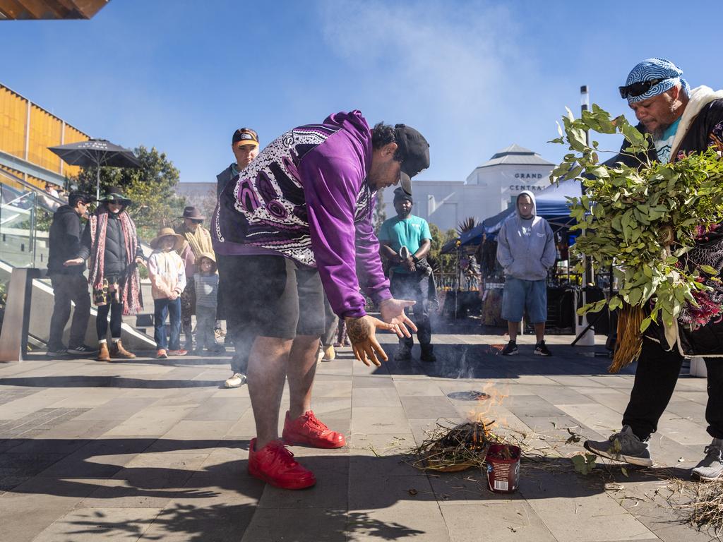 Jakiah Hill (left) lets the smoke waft over him as Jarowair Wakka Wakka man Conrad Bauwens conducts a Smoking Ceremony at the NAIDOC arts and craft market at Grand Central, Saturday, July 9, 2022. Picture: Kevin Farmer