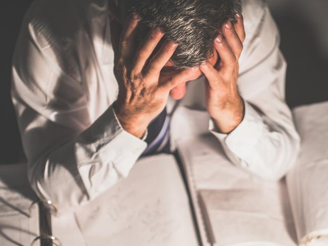 Senior businessman working in his office late at night alone. He is having some problems, he looks worried.