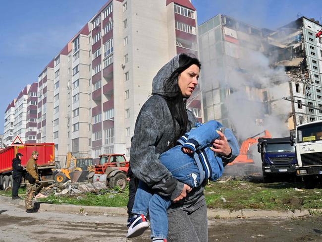 A woman walks past damaged residential buildings as she carries a child in Uman. Two children were among the dead. Picture: AFP