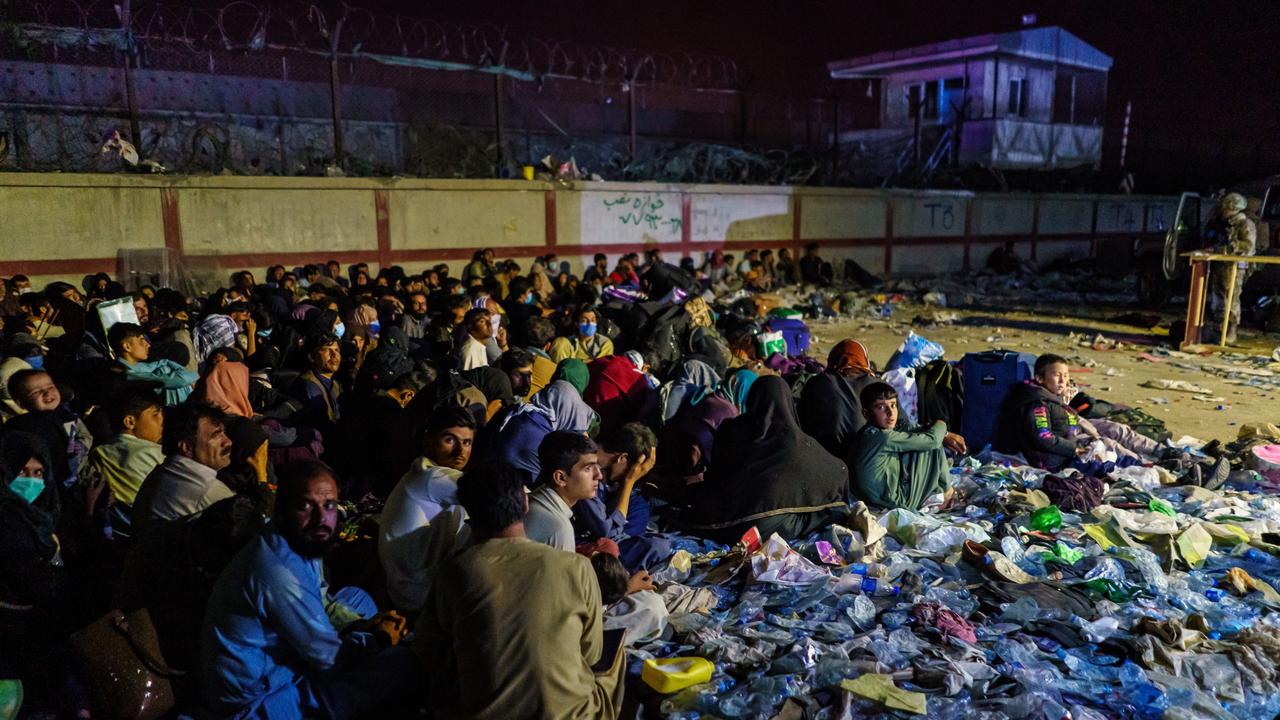 Afghan refugees crouch in a group as British military secure the perimeter outside the Baron Hotel, near the Abbey Gate, in Kabul, Afghanistan. Picture: LA Times