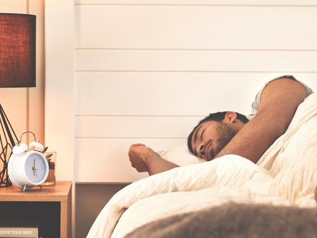 Man sleeping alone in cozy bedroom. Attractive young male resting comfortably in a soft bed with warm blankets. One tired hispanic person with closed eyes dreaming peacefully inside at night.