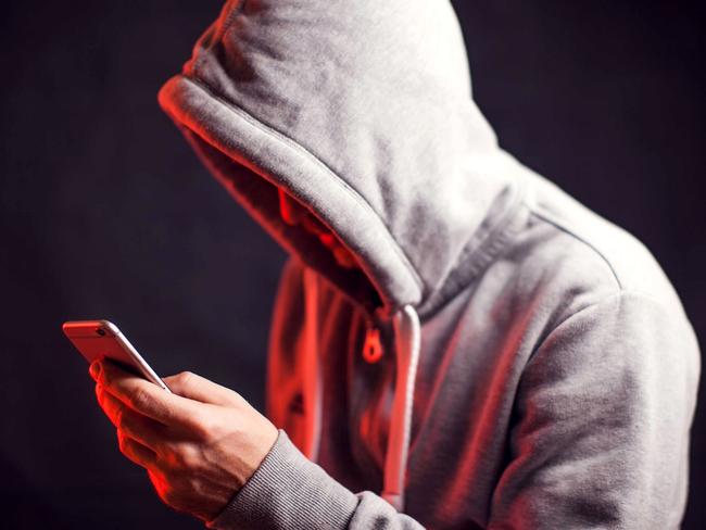 Man wearing hoody sweater with mobile phone in hands. Crime and hacking concept; scam generic.