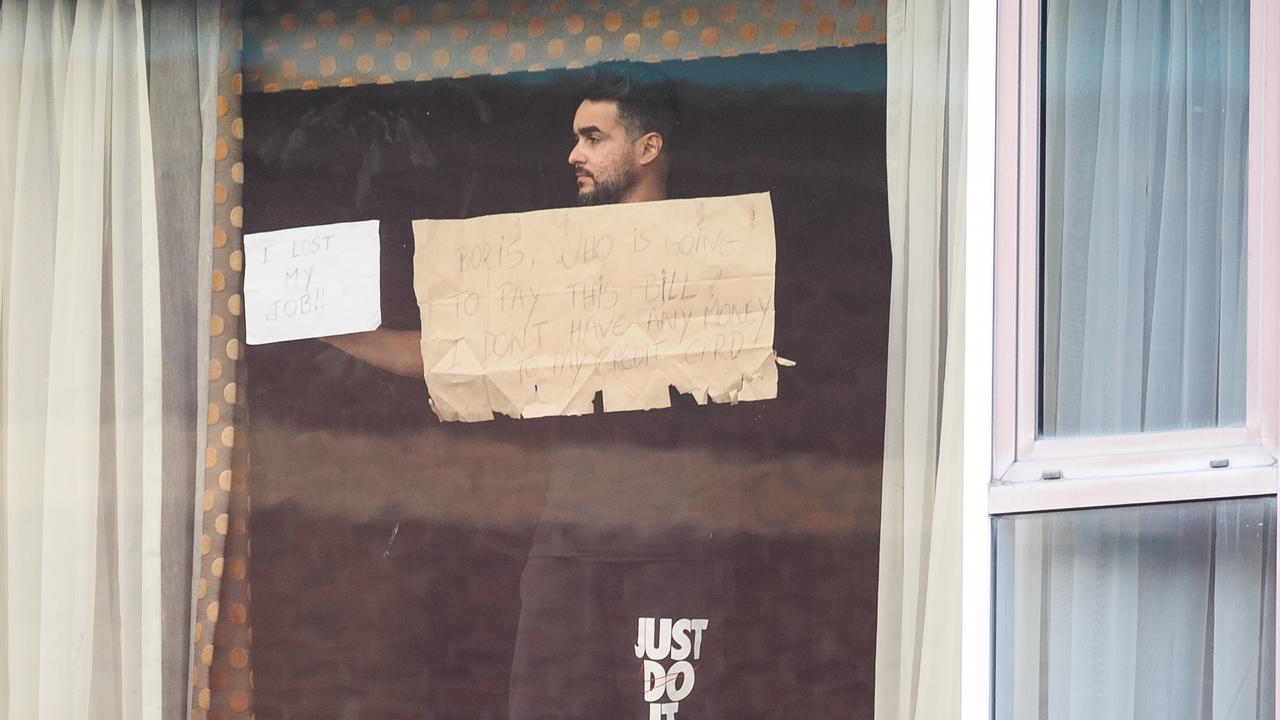 A man holds up signs reading "I LOST MY JOB!!" and "BORIS, WHO IS GOING TO PAY THIS BILL? I DON'T HAVE ANY MONEY TO PAY MY CREDIT CARD" at the window of his hotel room. Picture: Leon Neal/Getty Images.