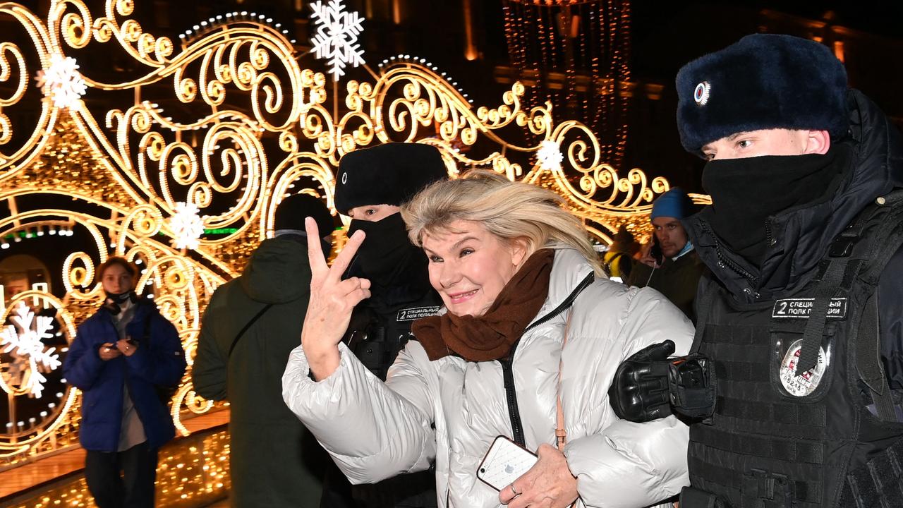 A woman gives the two finger salute as she’s led away by police. Picture: Kirill KUDRYAVTSEV / AFP