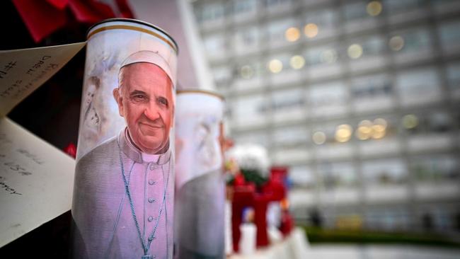 A candle with a portrait of Pope Francis is set at the bottom of a statue of Pope John Paul II outside the Gemelli hospital where Pope Francis is hospitalised for tests. Photo by Tiziana FABI / AFP