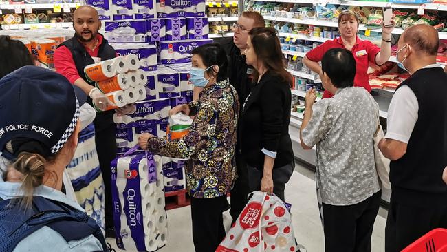 In Victoria, a police officer looks on as rolls of toilet paper are given to shoppers at a Coles supermarket Picture: James Gourley/ AAP