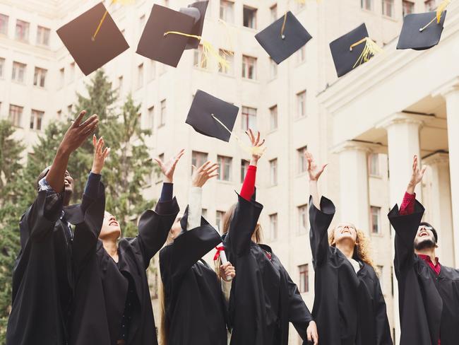 A group of multietnic students celebrating their graduation by throwing caps in the air. Education, qualification and gown concept.